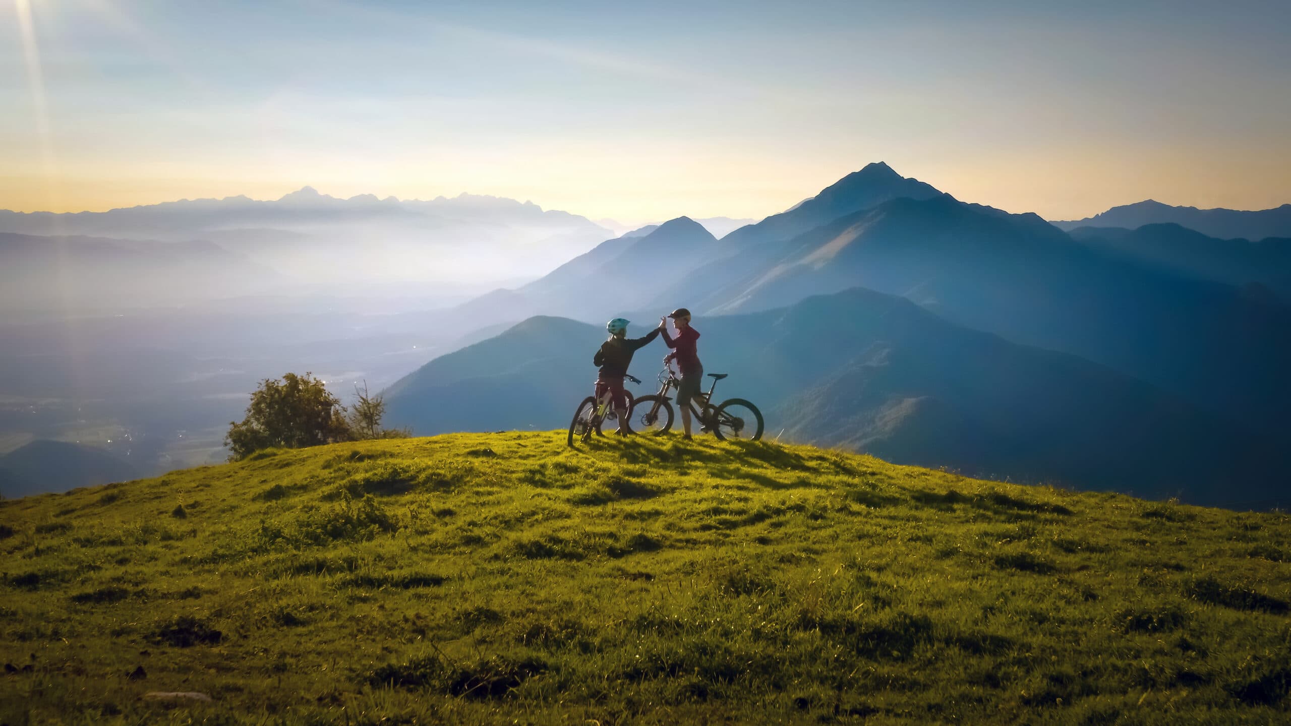 Zwei glückliche Frauen geben sich nach einer erfolgreichen Mountainbike-Tour in den Bergen beim Sonnenuntergang ein High Five.
