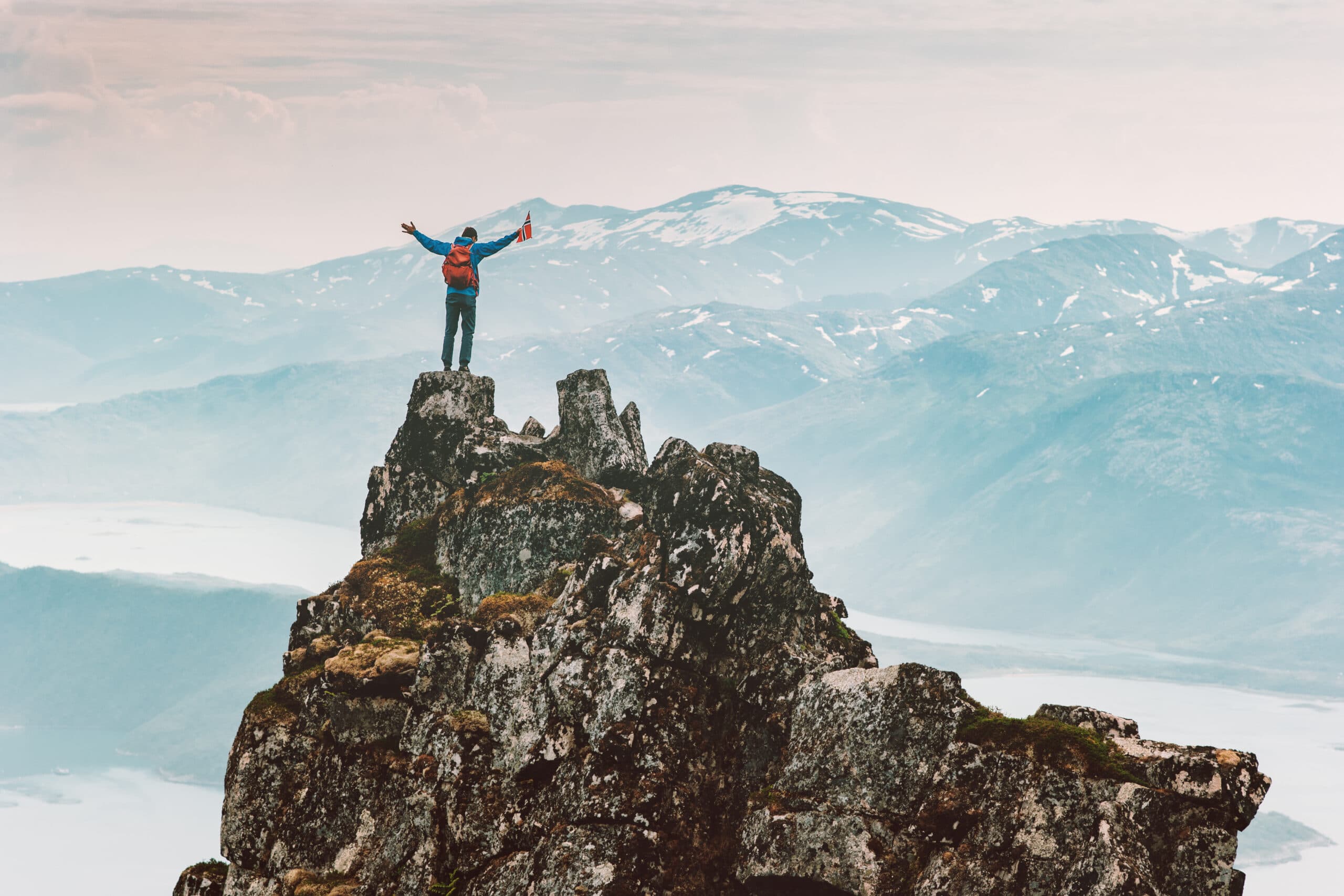 Mann steht triumphierend auf einem schroffen Berggipfel im Sonnenschein