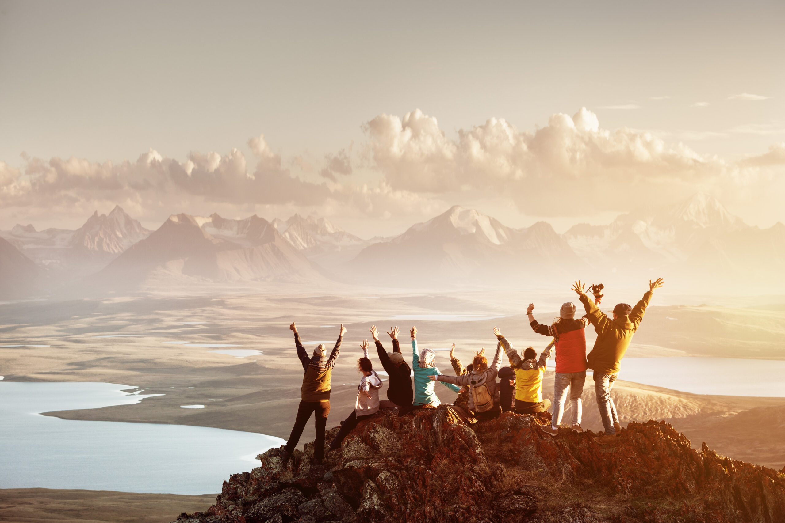 Eine Gruppe junger Freunde jubelt beim Sonnenaufgang auf einem Felsen vor Gebirgslandschaft