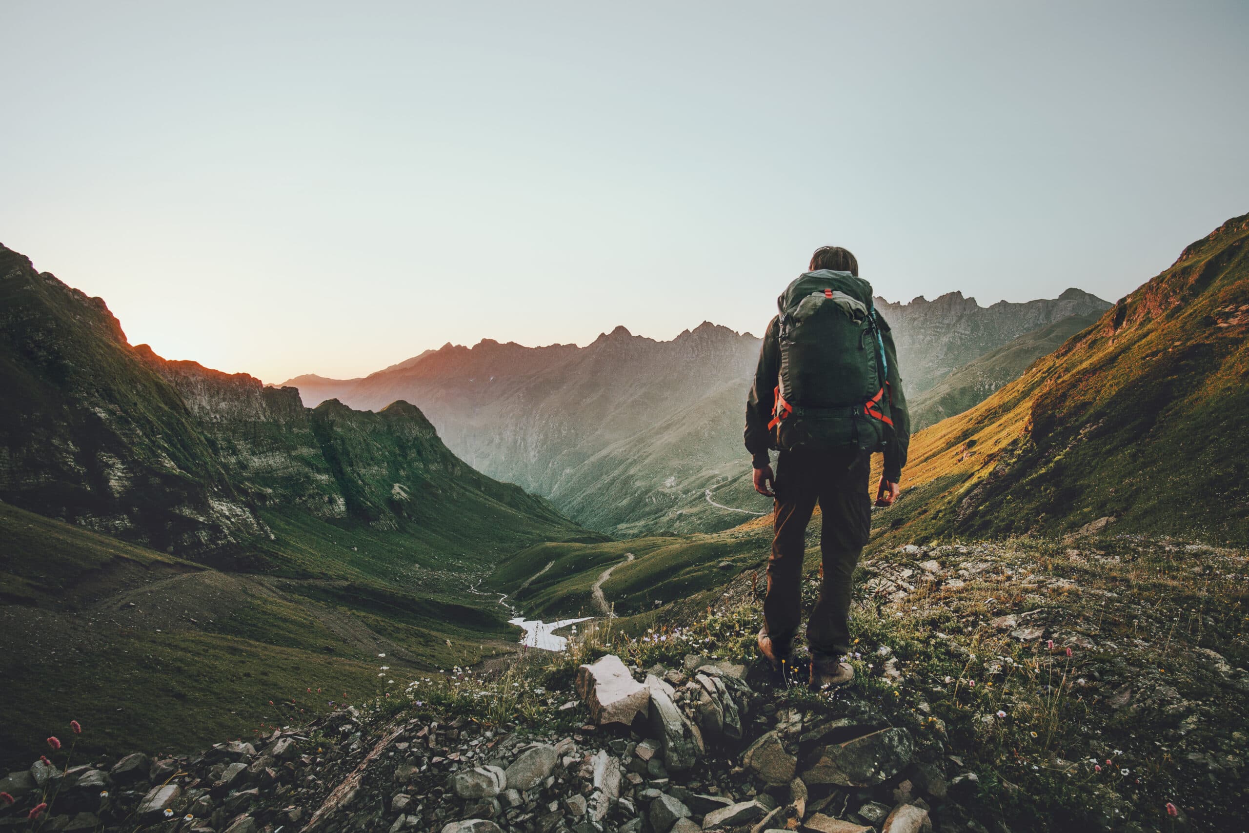 Ein Mann mit Rucksack steigt einen Berg hinauf und blickt ins Tal